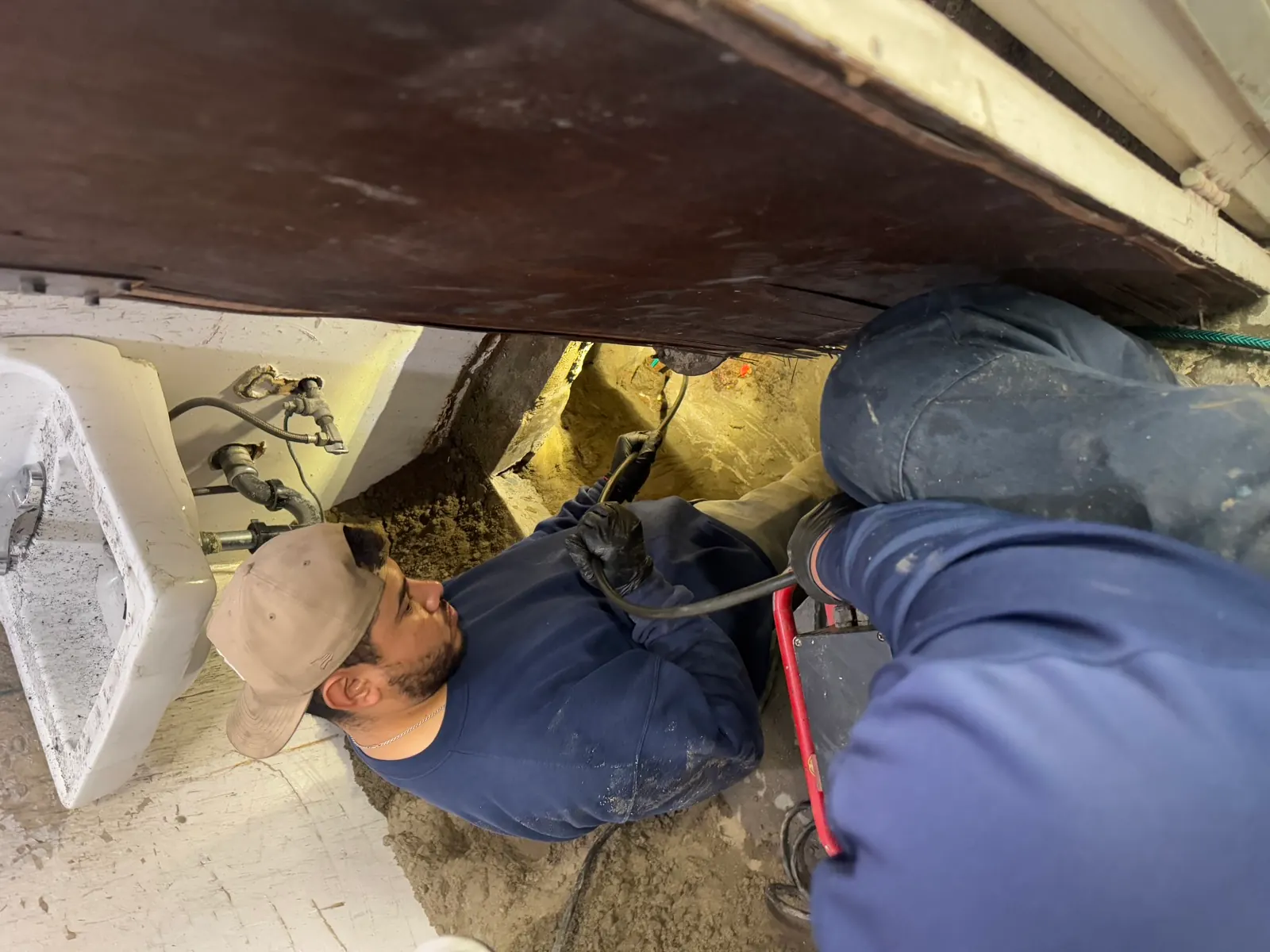 Trifecta technician running a drain cable machine at an opened floor beside a commercial utility sink